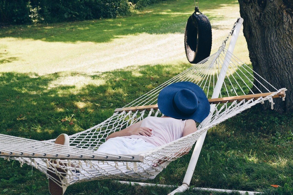 Woman lays in hammock above a trimmed green lawn. BugOut offers summer lawn care for mid-Missouri homeowners.